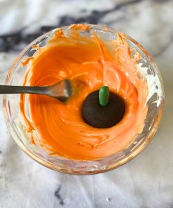 dip pumpkin shaped Oreo ball in melted orange chocolate