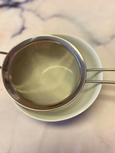 place strainer over a bowl to strain raspberry puree for buttercream frosting