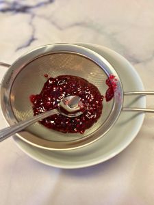 use the back of a spoon to push raspberry puree for buttercream frosting through a strainer