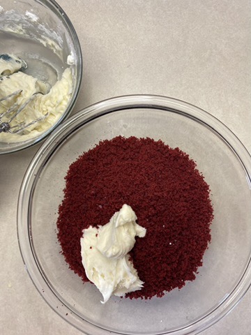 half a bowl of cream cheese frosting. The other half of the cream cheese frosting is in a bowl of red velvet cake crumbs