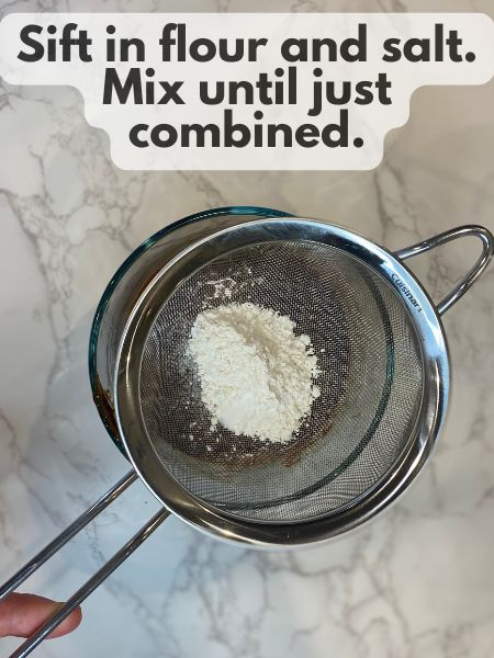 a strainer with flour and salt over a bowl of lava cake batter sifting the flour and salt into the batter