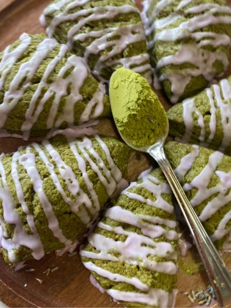 matcha scones with lavender glaze arranged in a circle with a spoon full of matcha resting on them