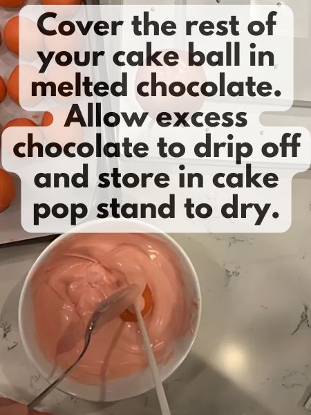 strawberry cake ball on a stick in a bowl of melted pink chocolate while a spoon gently covers the cake ball in chocolate