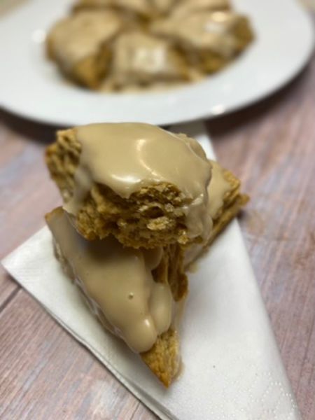 vegan maple scones sitting on a napkin. one scone has a bite taken out of it revealing a flaky interior