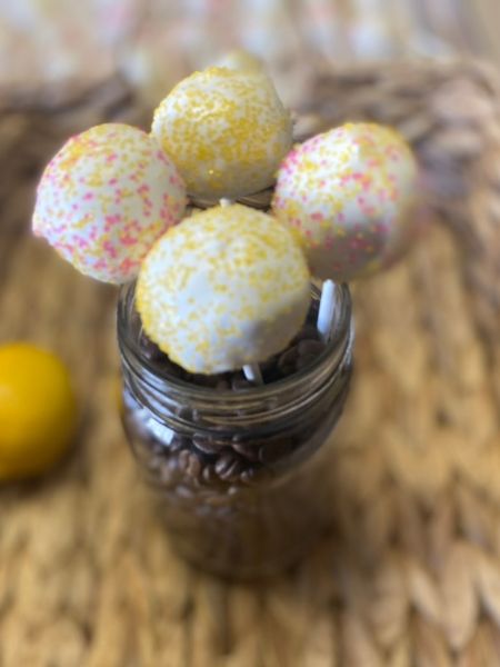 lemon cake pops decorated with white chocolate coating and yellow and pink sprinkles