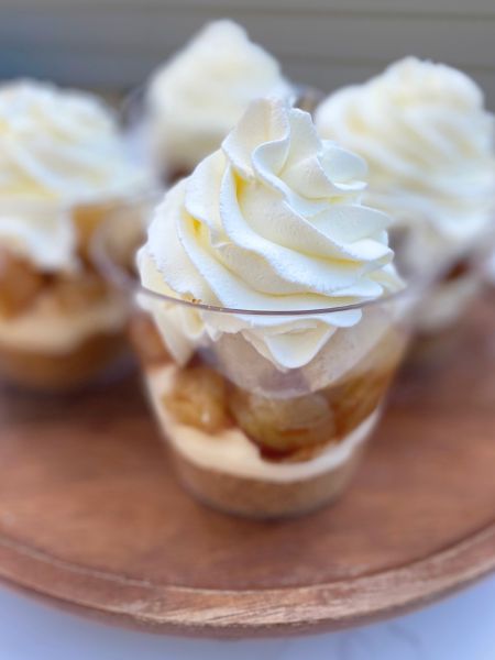 a clear cup with a layer of graham cracker crumbs, cheesecake filling and apple pie filling topped with whipped cream