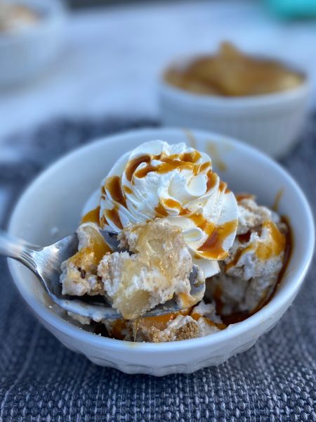 ice cream with chunks of apple pie filling covered in whipped cream and drizzled in caramel