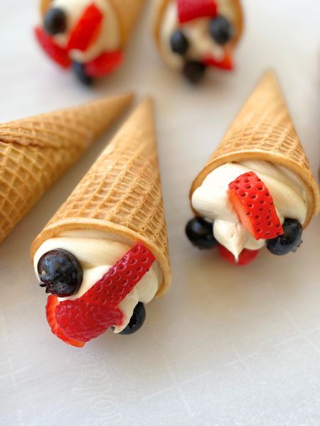ice cream cones filled with a swirl of cheesecake filling and topped with blueberries, strawberries and raspberries