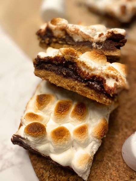 a stack of bars with a graham cracker crust, chocolate ganache filling and topped with toasted mini marshmallows