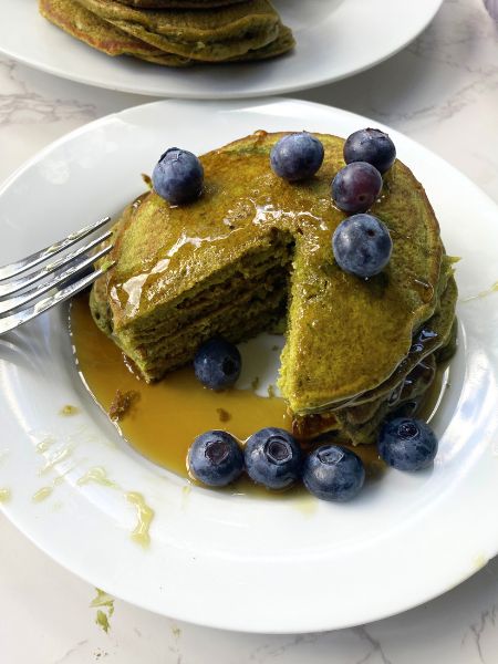 matcha pancakes on a plate drizzled in syrup and with blueberries on top