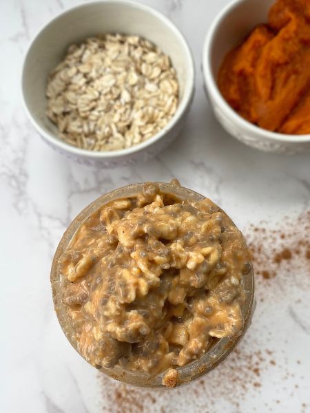 pumpkin overnight oats with cookie butter in a jar next to bowls of oats and pumpkin puree