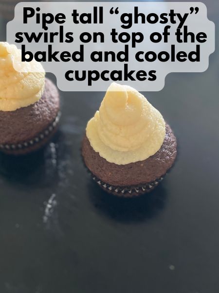 vanilla buttercream piped into ghost shapes on top of chocolate cupcakes