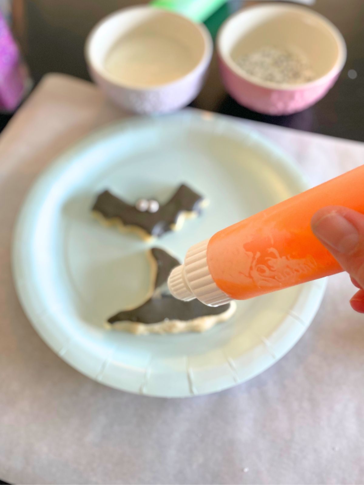 someone decorating a Halloween sugar cookies with a small piping bottle