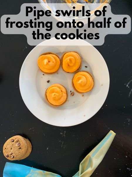 buttercream frosting piped in swirls on top of chocolate chip cookies