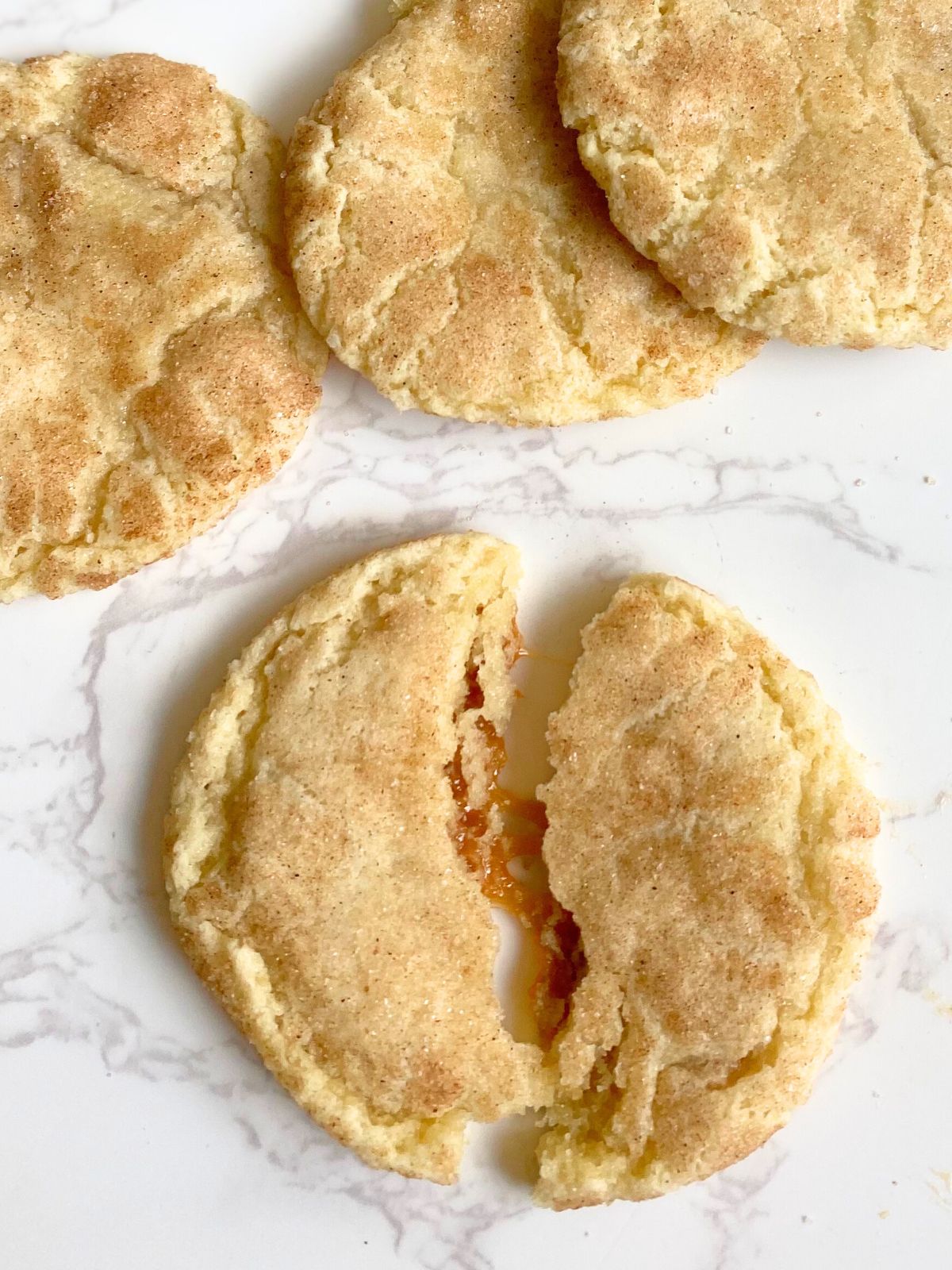 caramel stuffed snickerdoodle broken in half with caramel oozing out the middle