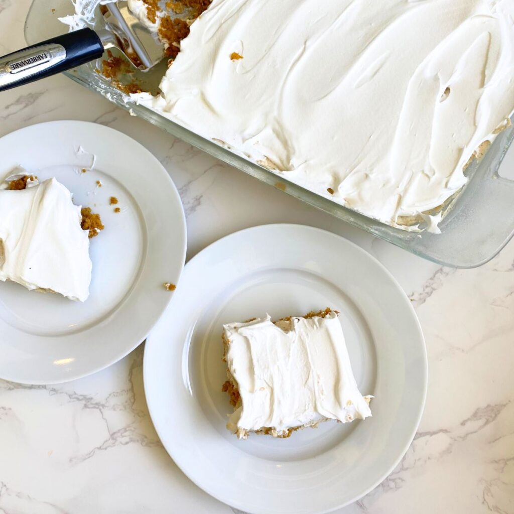 a slice of pumpkin poke cake with brown butter maple frosting on a plate next to a larger container of cake