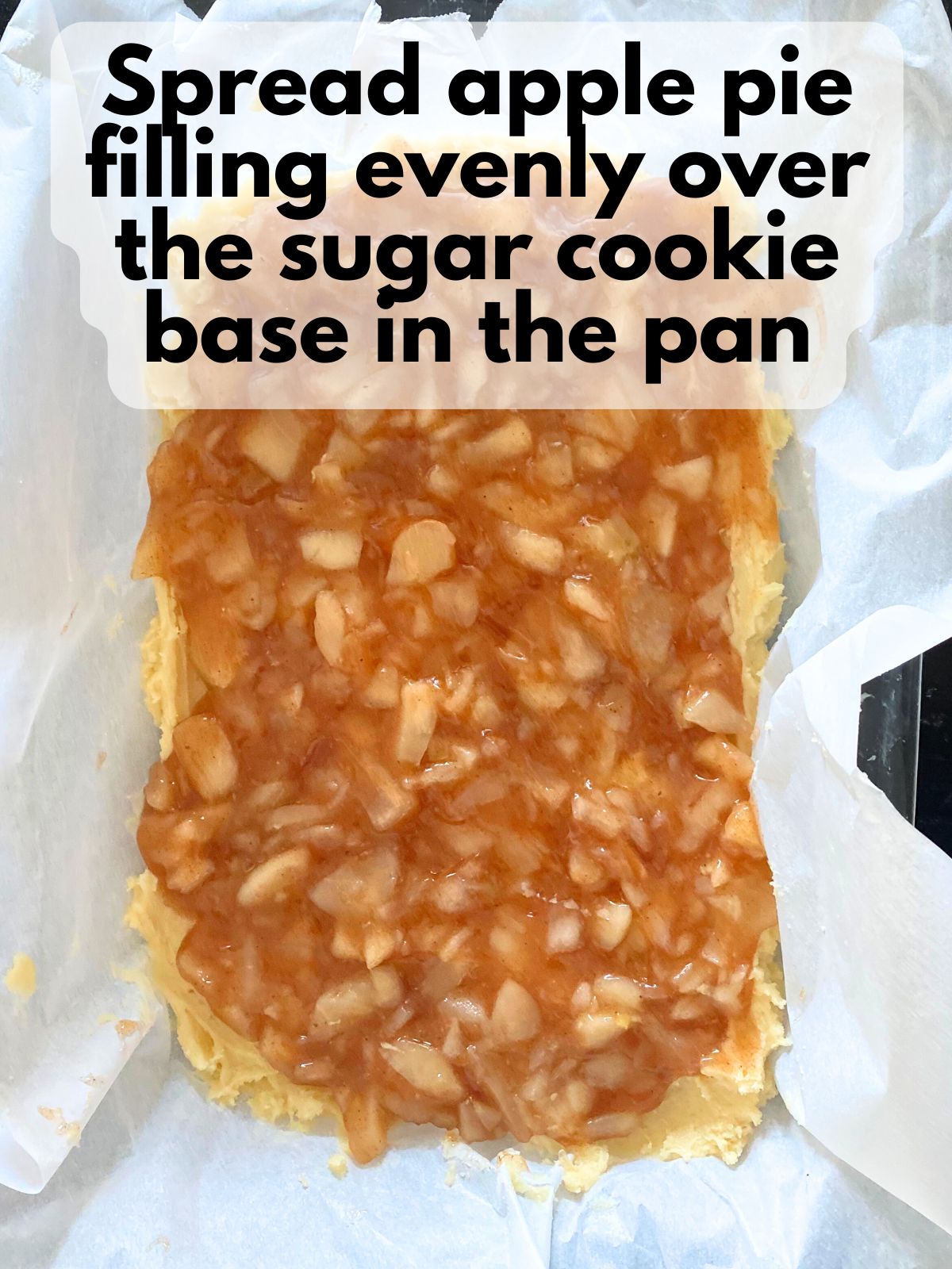 apple pie filling spread on top of sugar cookie dough in baking pan