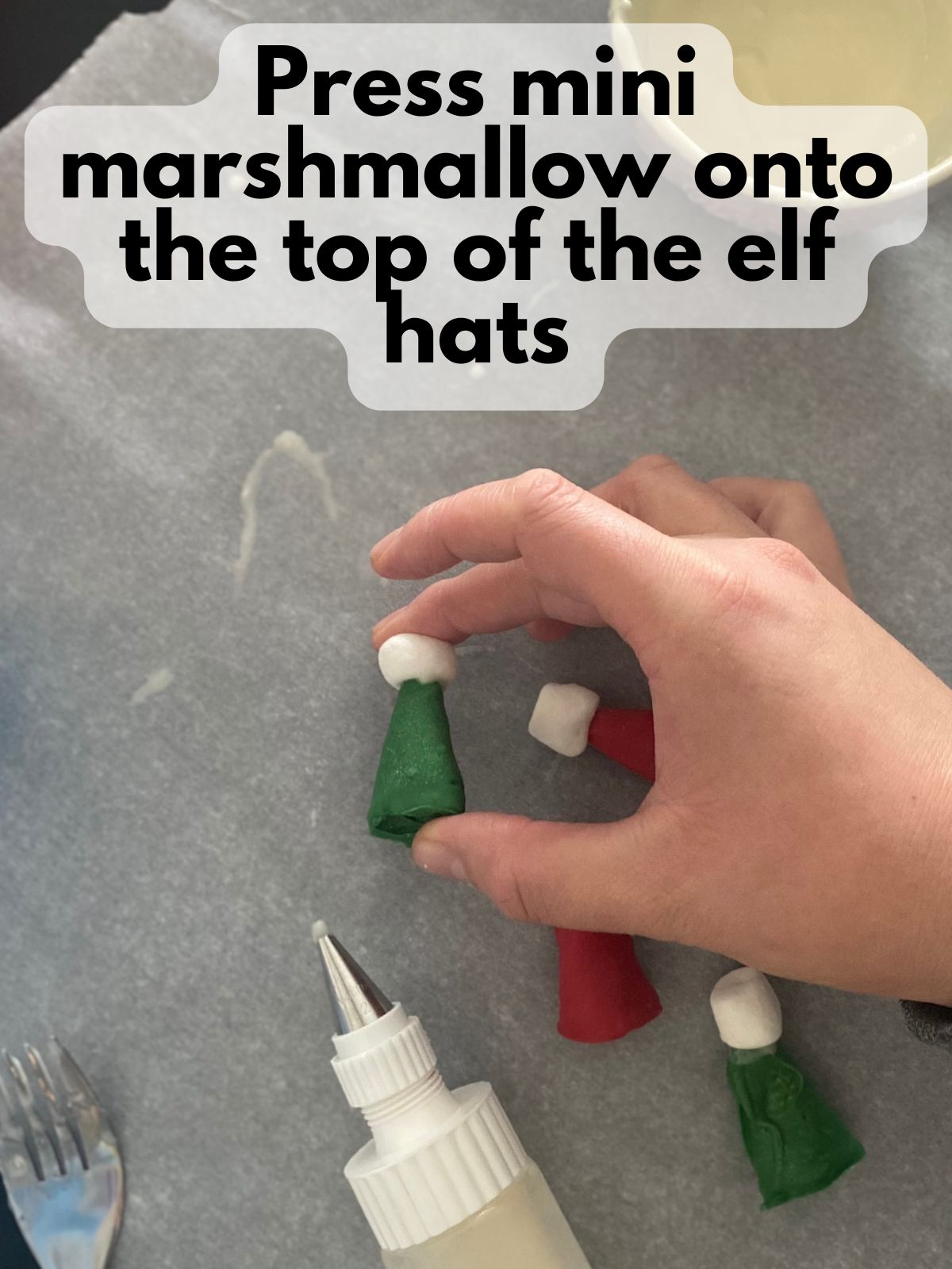 hand pressing mini marshmallow onto elf hat treat