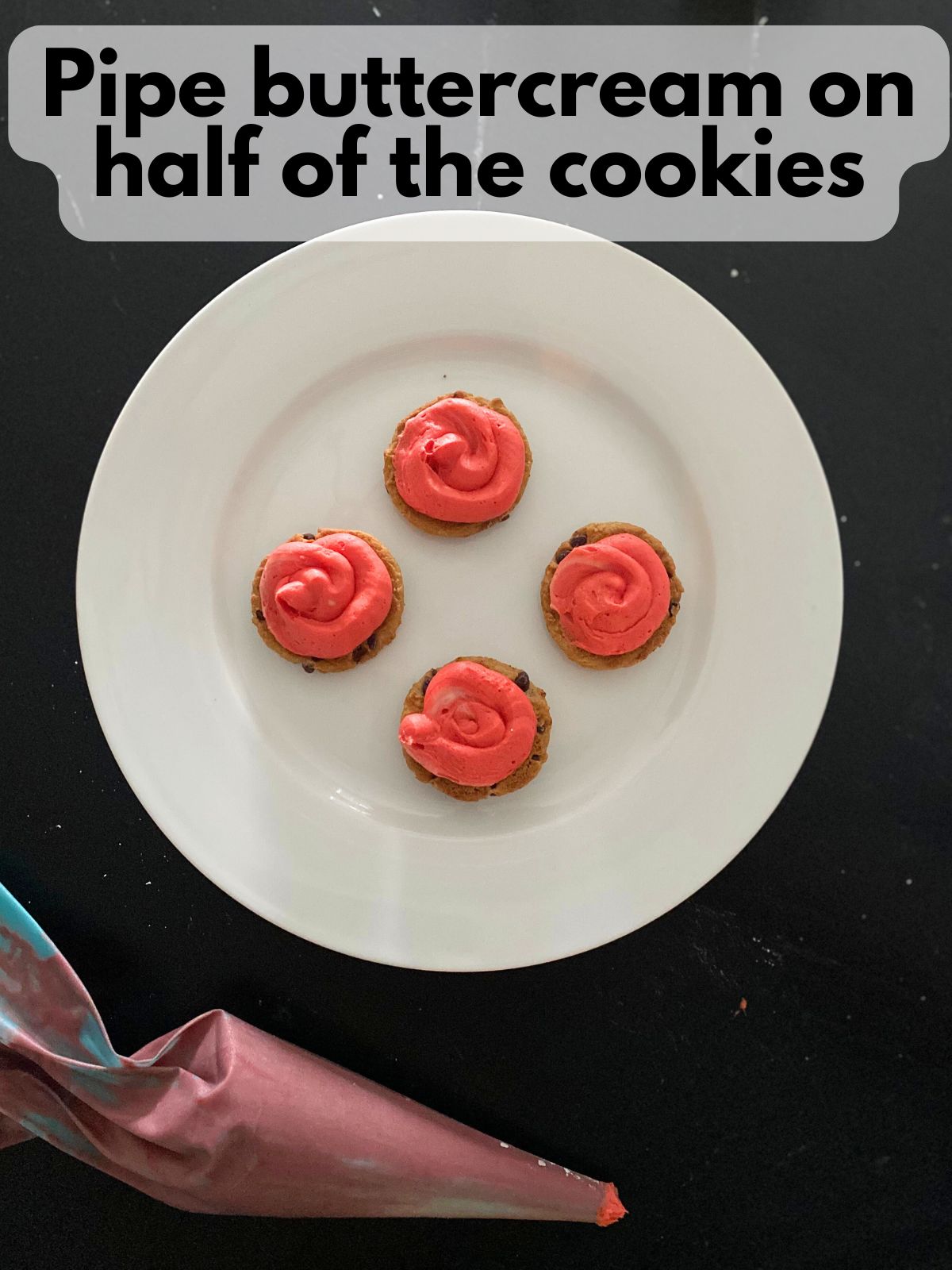 red buttercream frosting piped on top of chocolate chip cookies