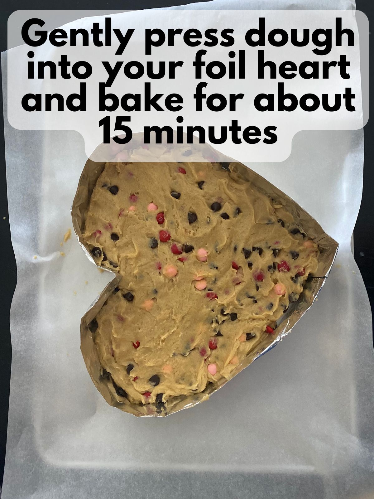 cookie cake dough pressed into an aluminum foil frame shaped like a heart