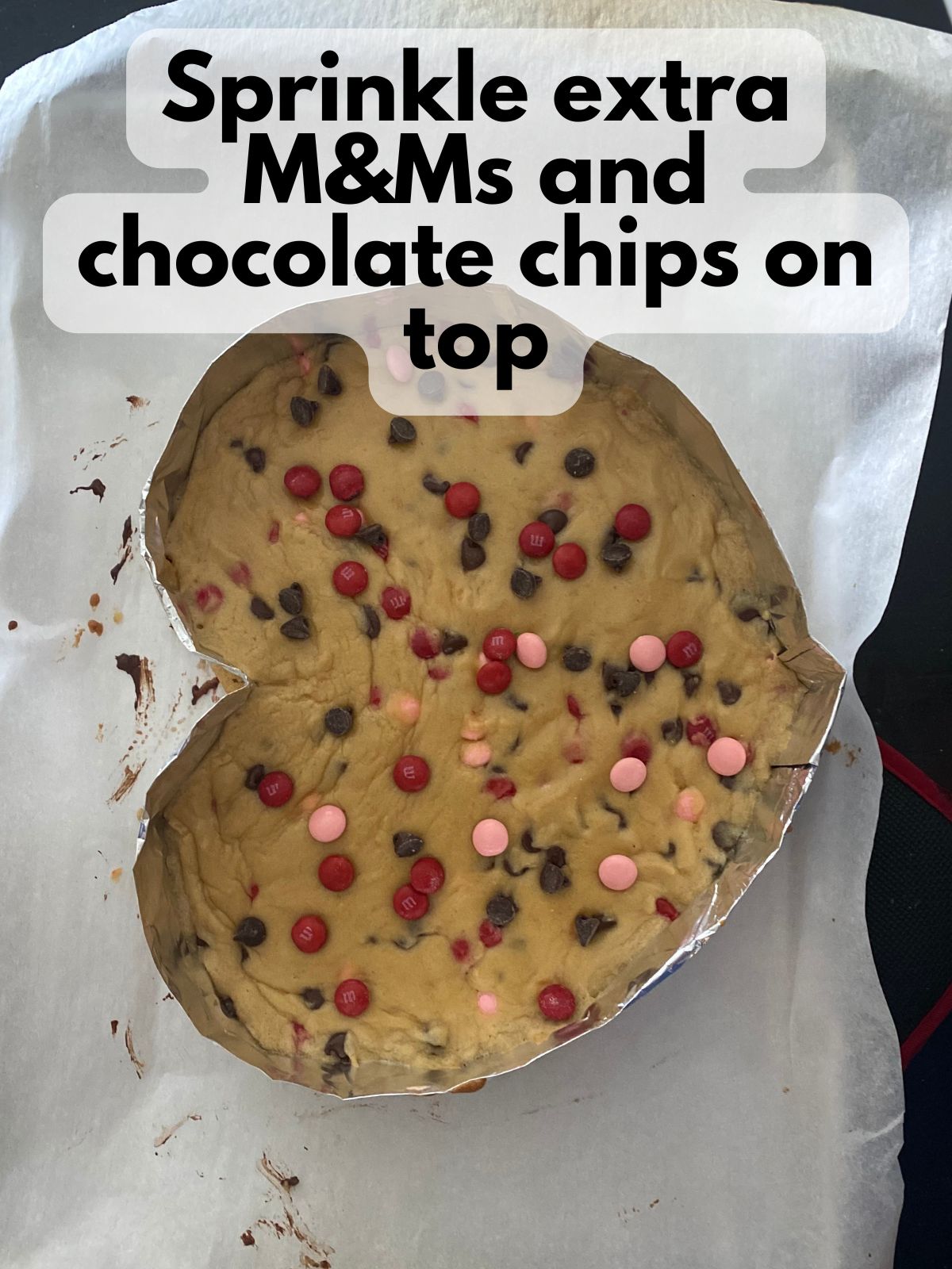 par-baked heart cookie cake with extra M&Ms and chocolate chips sprinkled on top