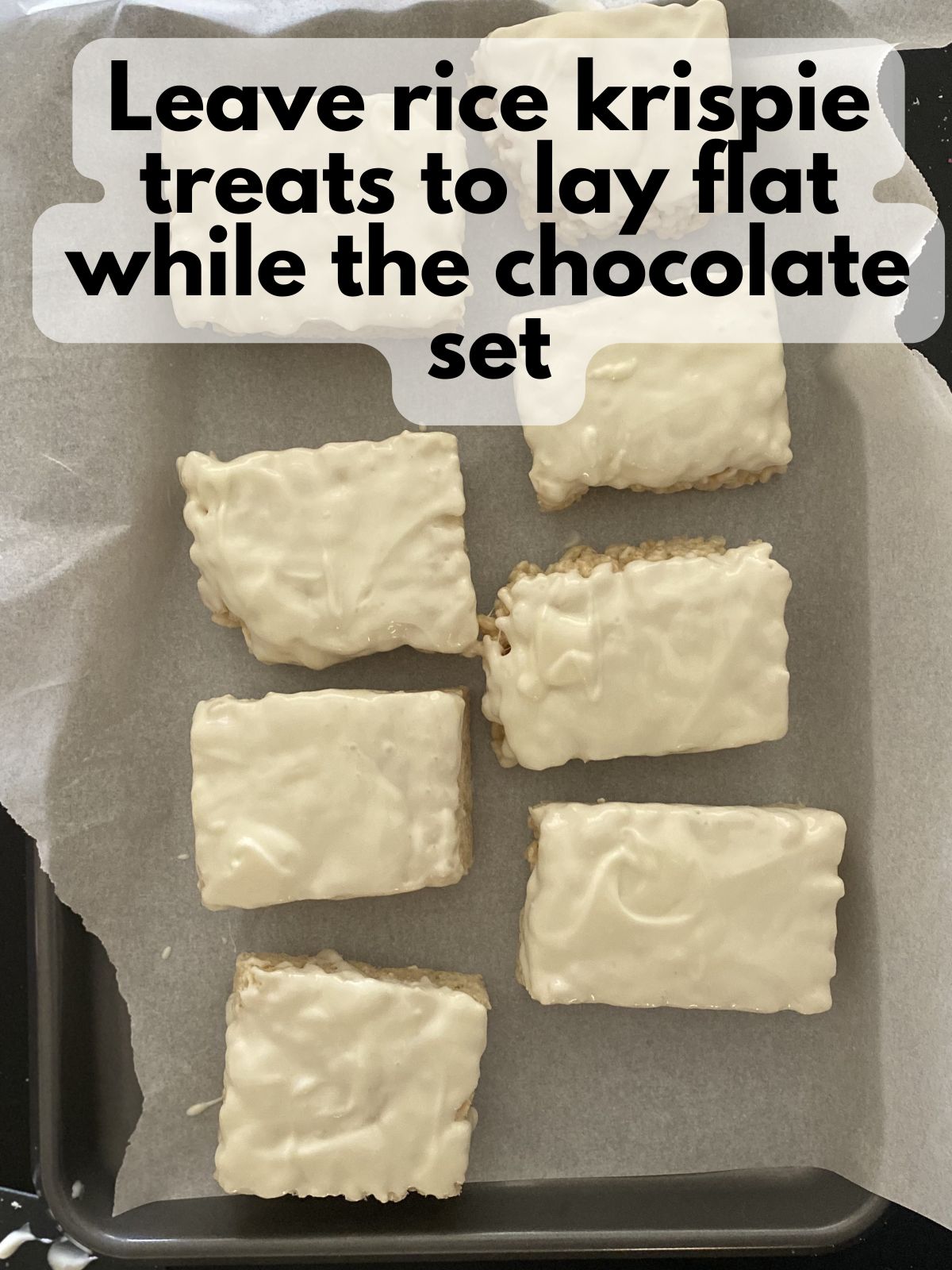 Rice krispie treats dipped in chocolate resting on a baking sheet lined with parchment paper