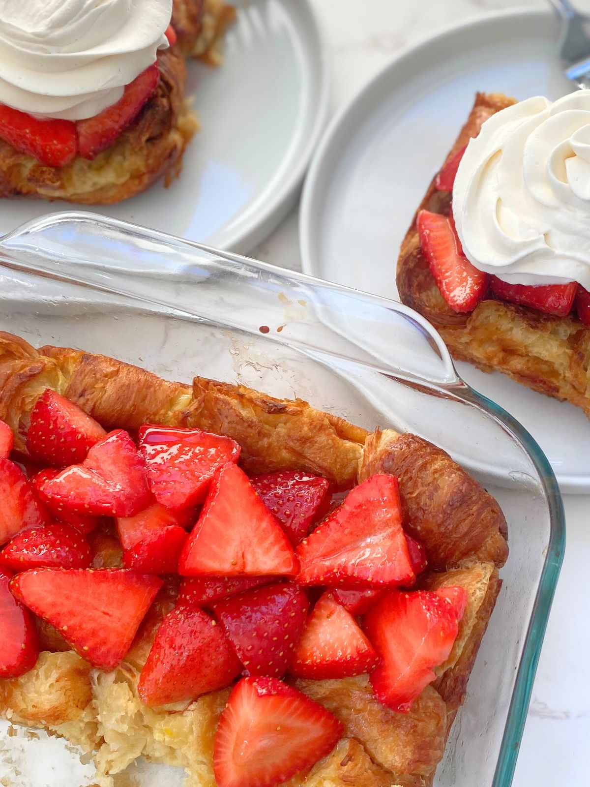 strawberry shortcake croissant bake in a baking dish and on a plate with whipped cream