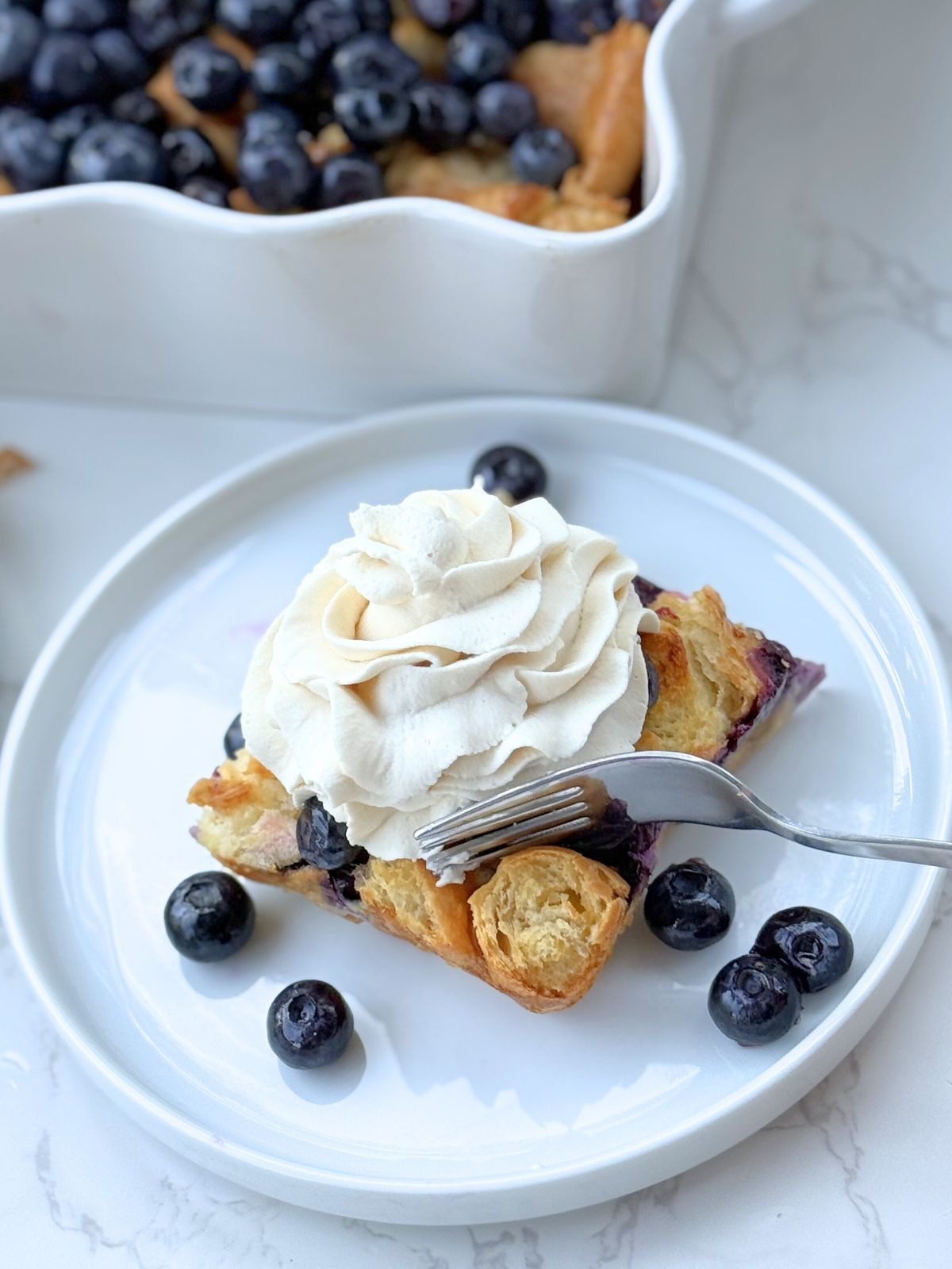 blueberry croissant bake on a plate with a bite being taken out of it