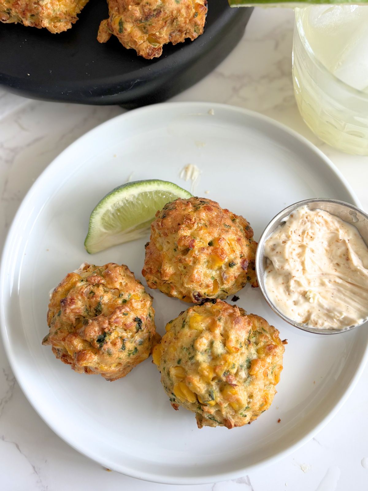 fried elote fritters on a plate next to a lime wedge and some chipotle mayo