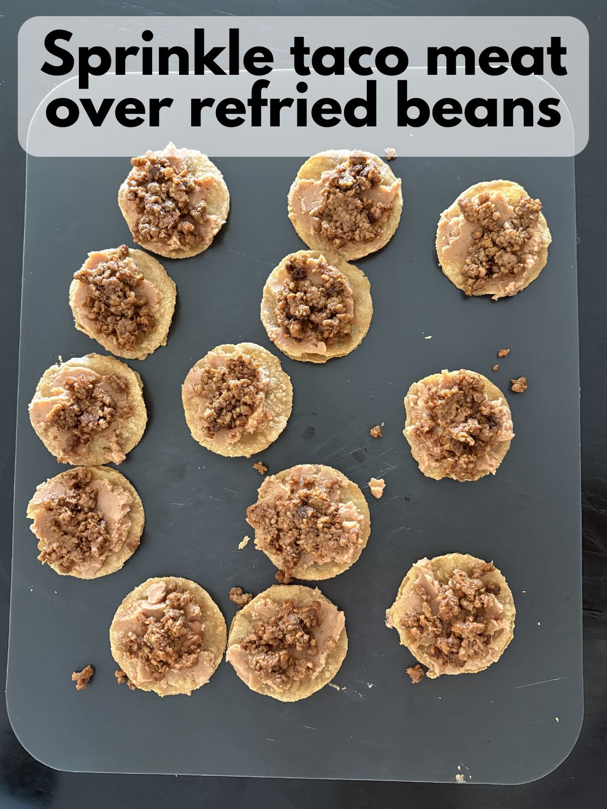 taco meat sprinkled on top of beans spread on tortillas