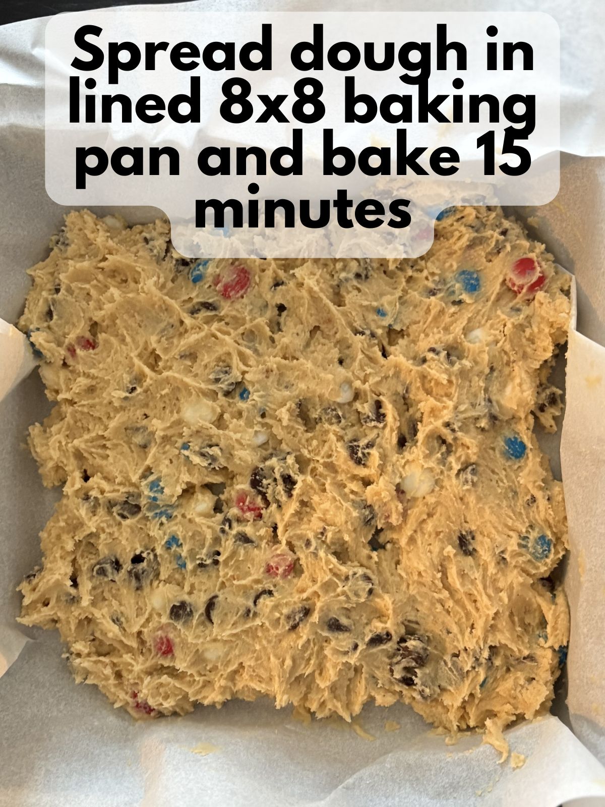 4th of July M&M cookie bar dough spread in an 8x8 pan lined with parchment paper