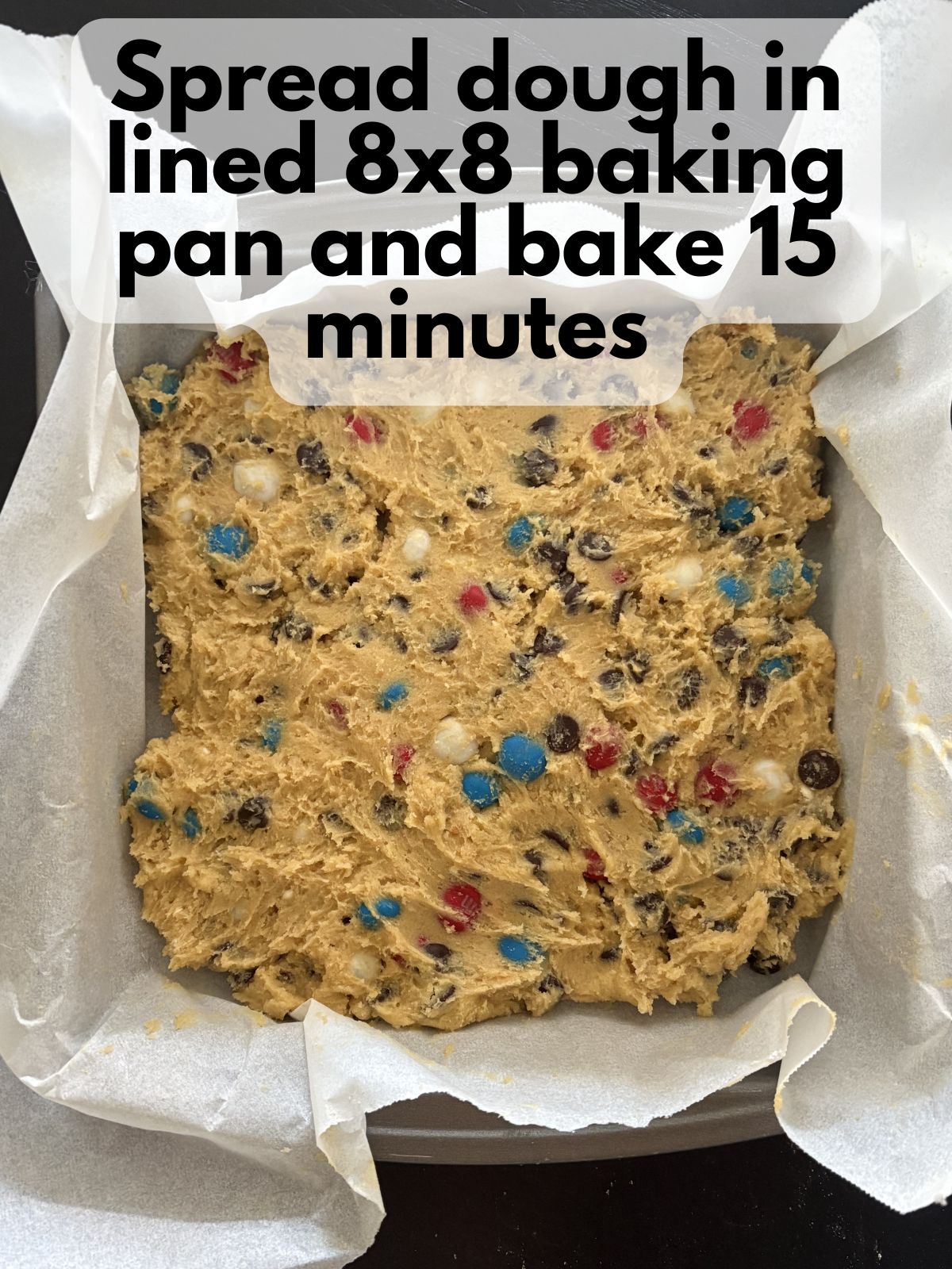 peanut butter M&M cookie bar dough spread in an 8x8 pan lined with parchment paper