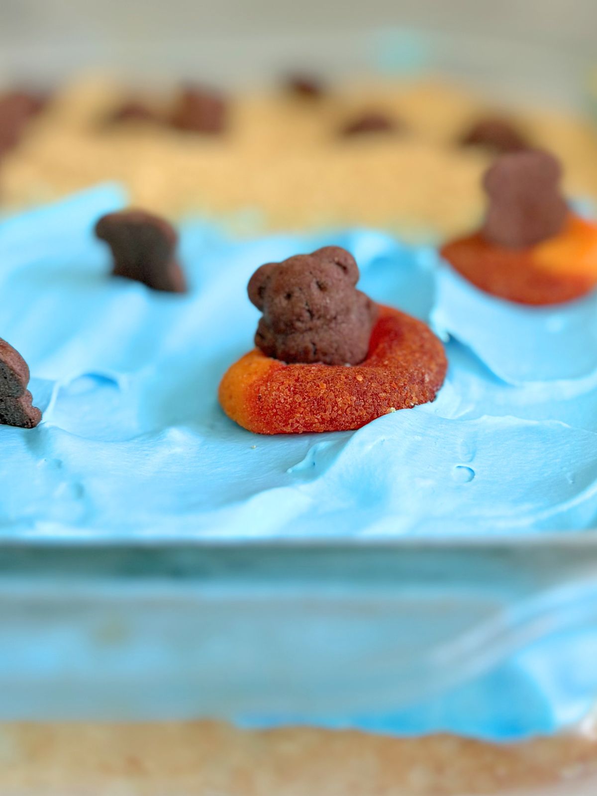 Teddy Graham in a peach ring "floatie" on top of beach poke cake
