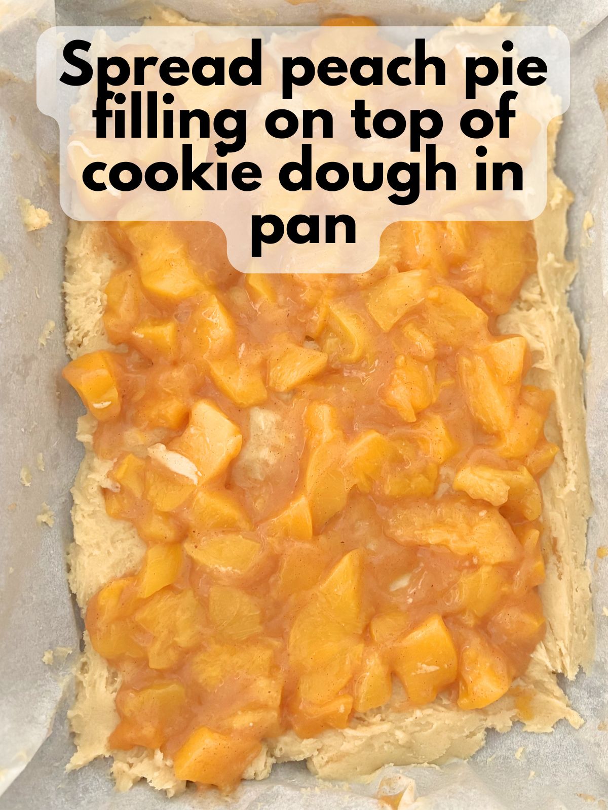 chopped peach pie filling spread over cookie dough in a 9x13 pan