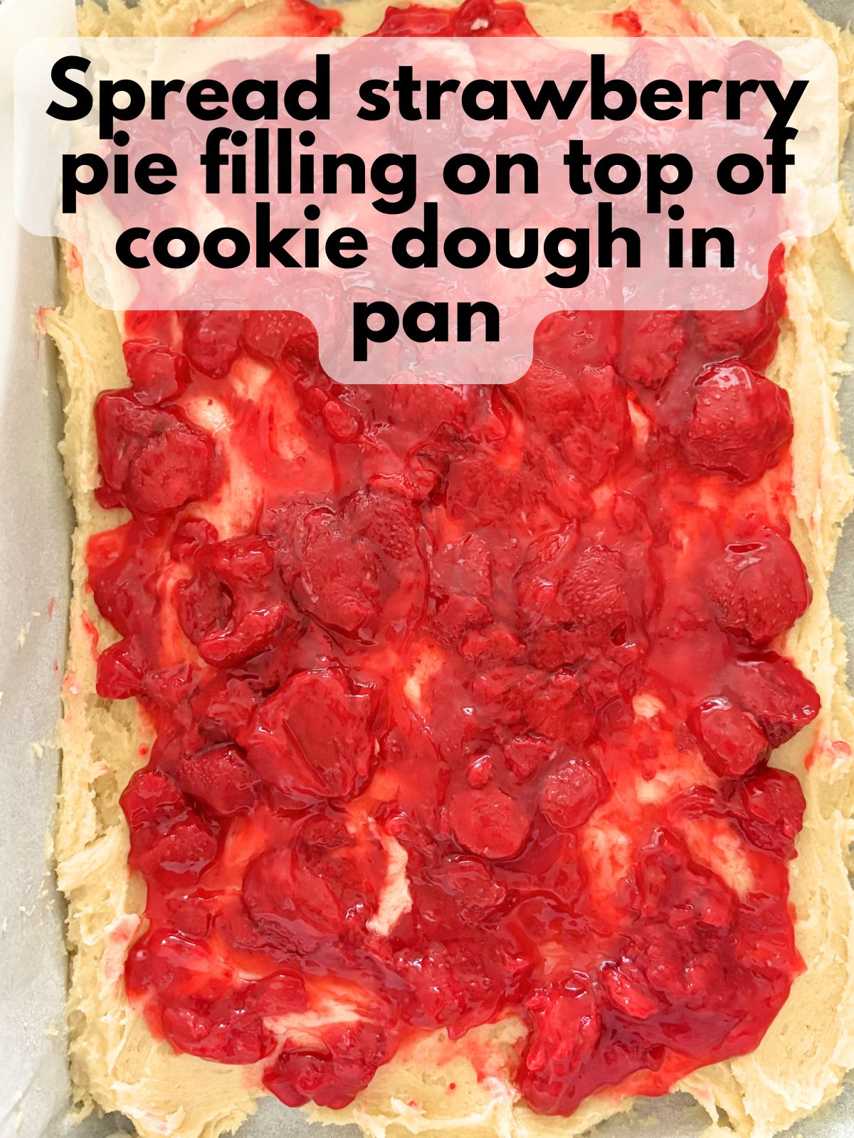 strawberry pie filing spread on top of sugar cookie dough in a 9x13 pan
