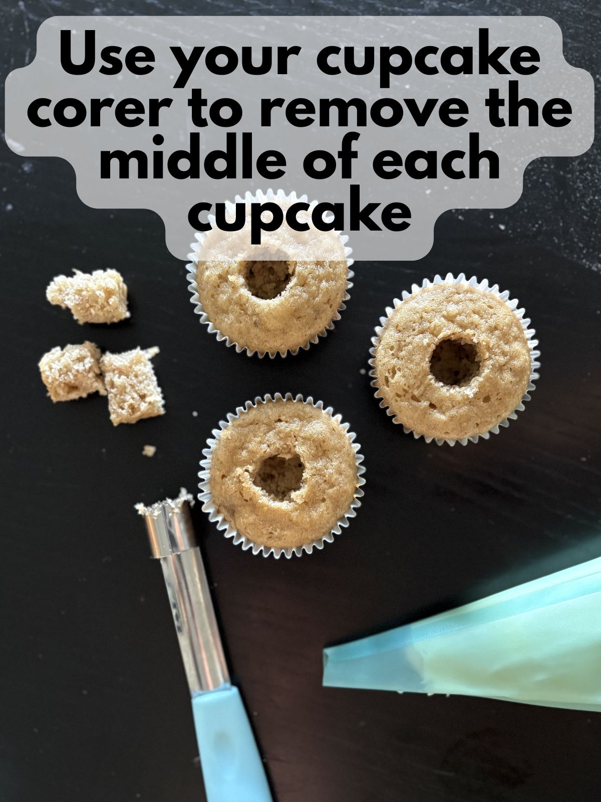 baked cupcakes with their centers removed, a cupcake corer and a piping bag with filling are sitting next to them