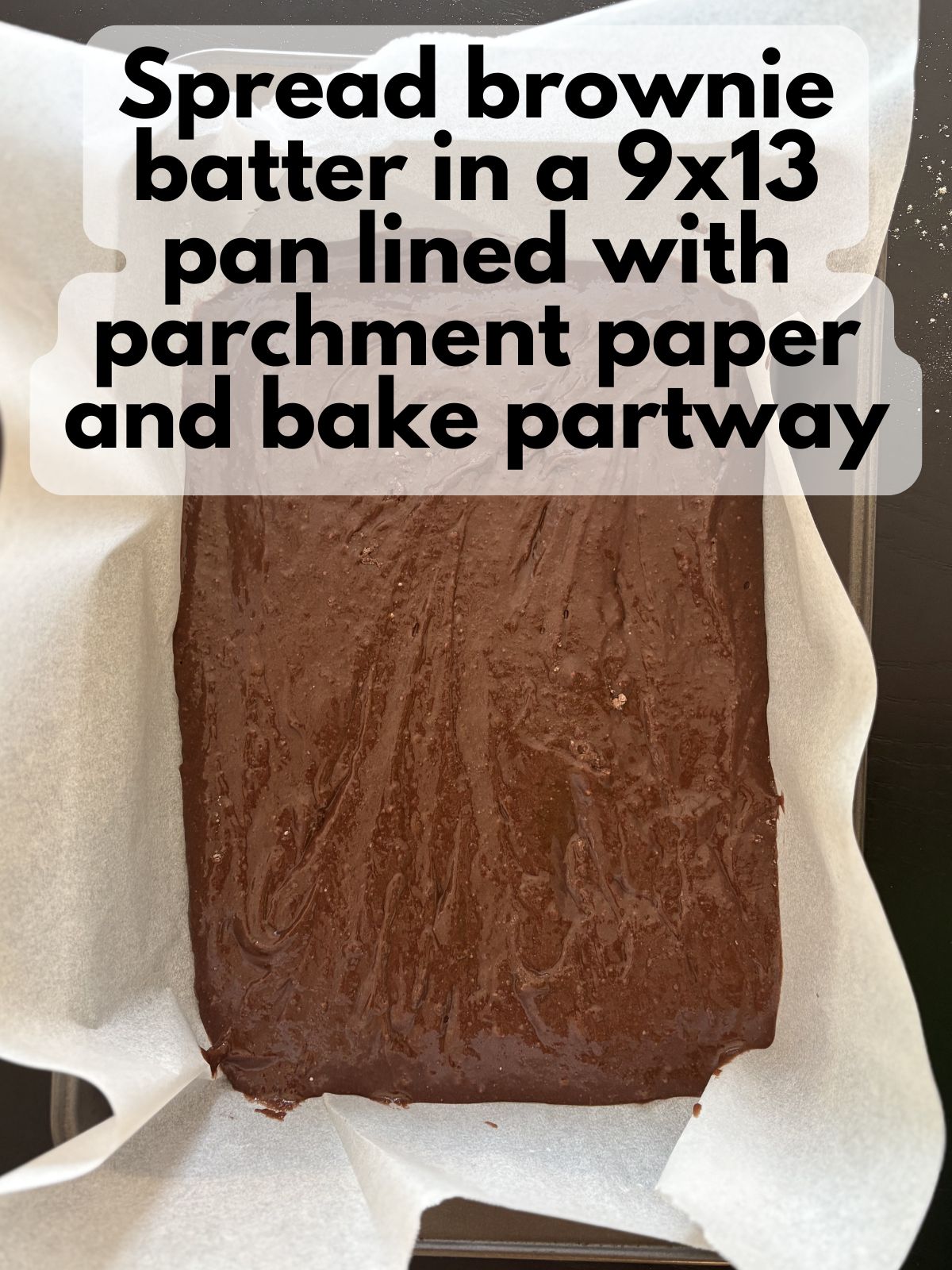 brownie batter spread in a 9x13 pan lined with parchment paper