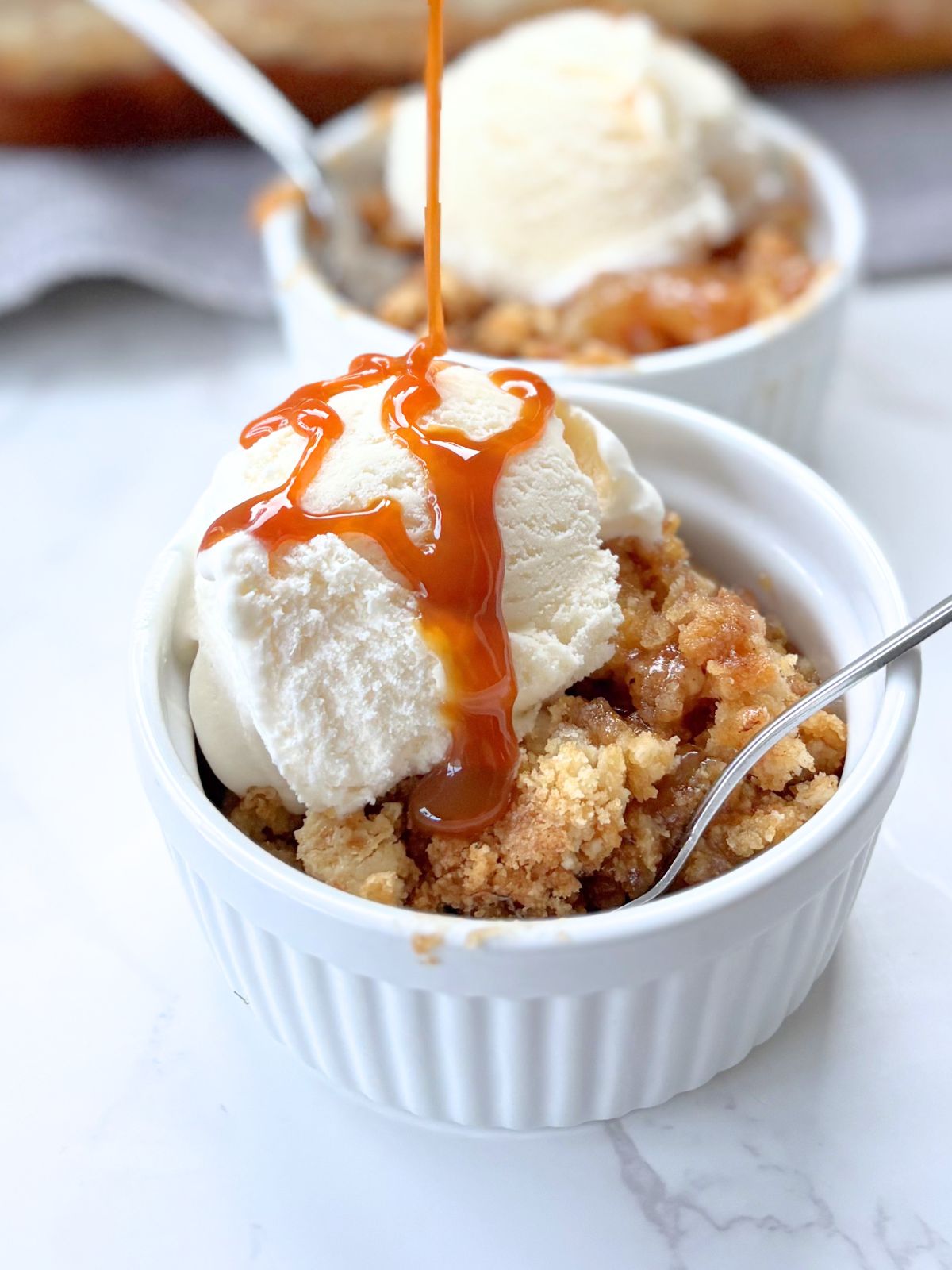 caramel being drizzled over a scoop of vanilla ice cream on top of a bowl of cake mix apple cobbler