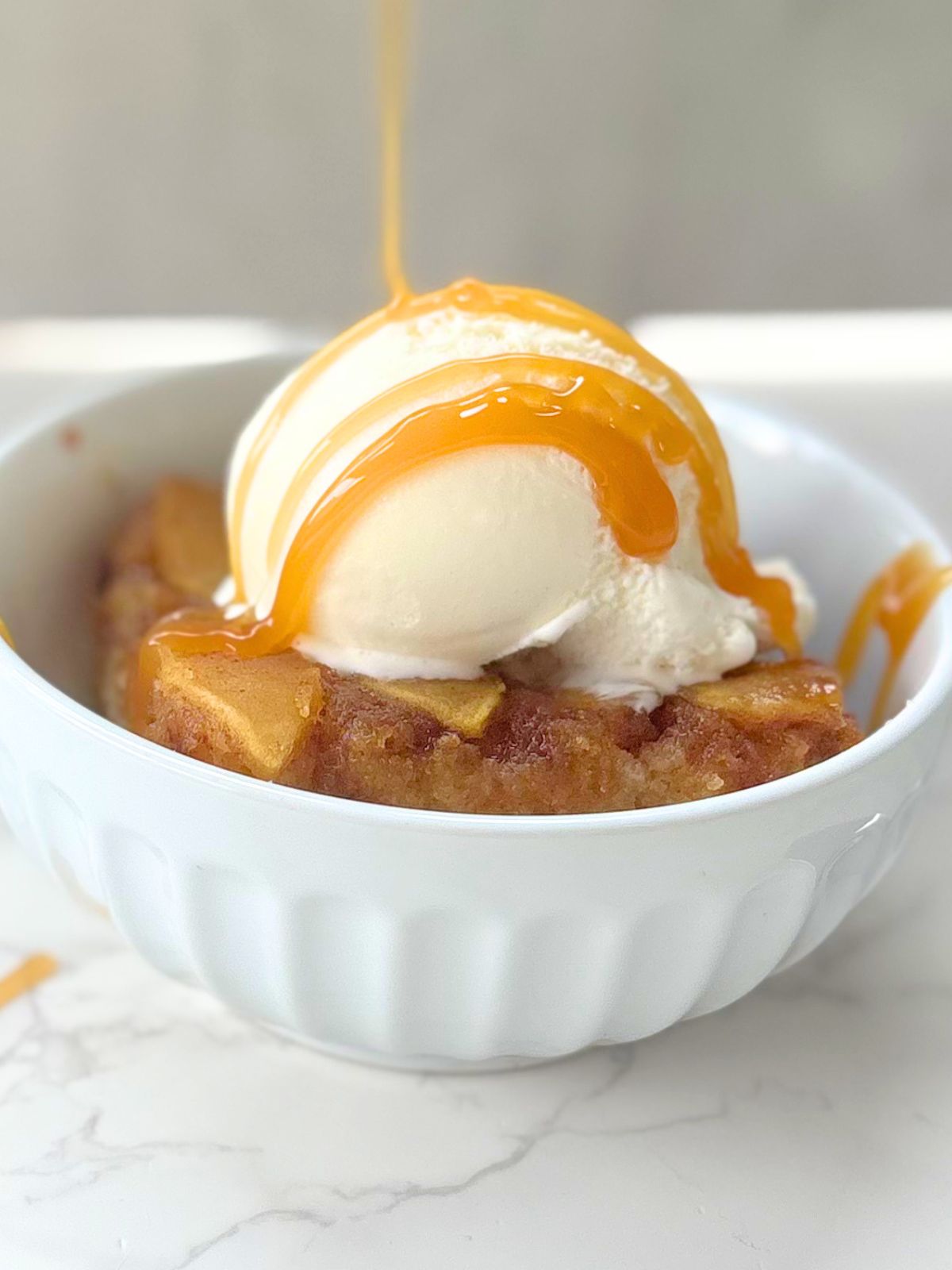 caramel being drizzled over a scoop of ice cream over a piece of apple upside down cake