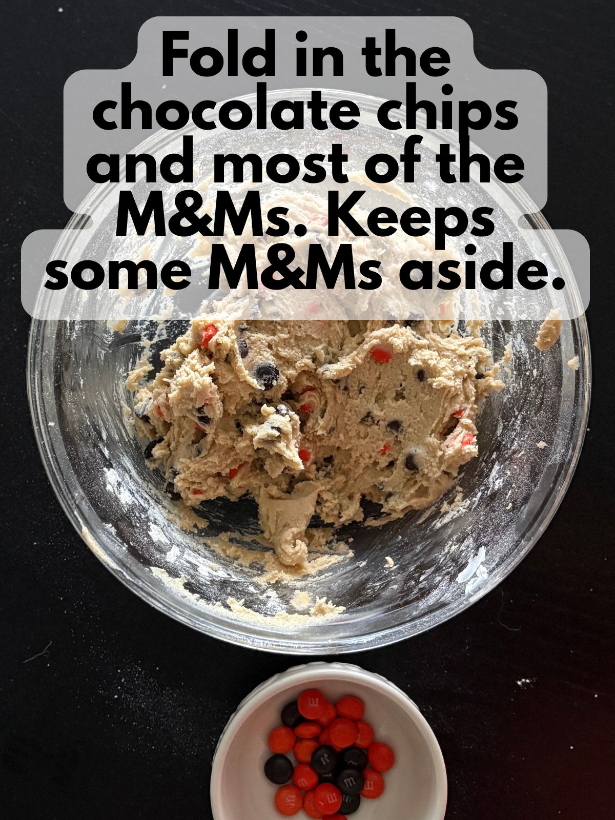 M&Ms and chocolate chips folded into cookie dough, some M&Ms are sitting to the side in a bowl