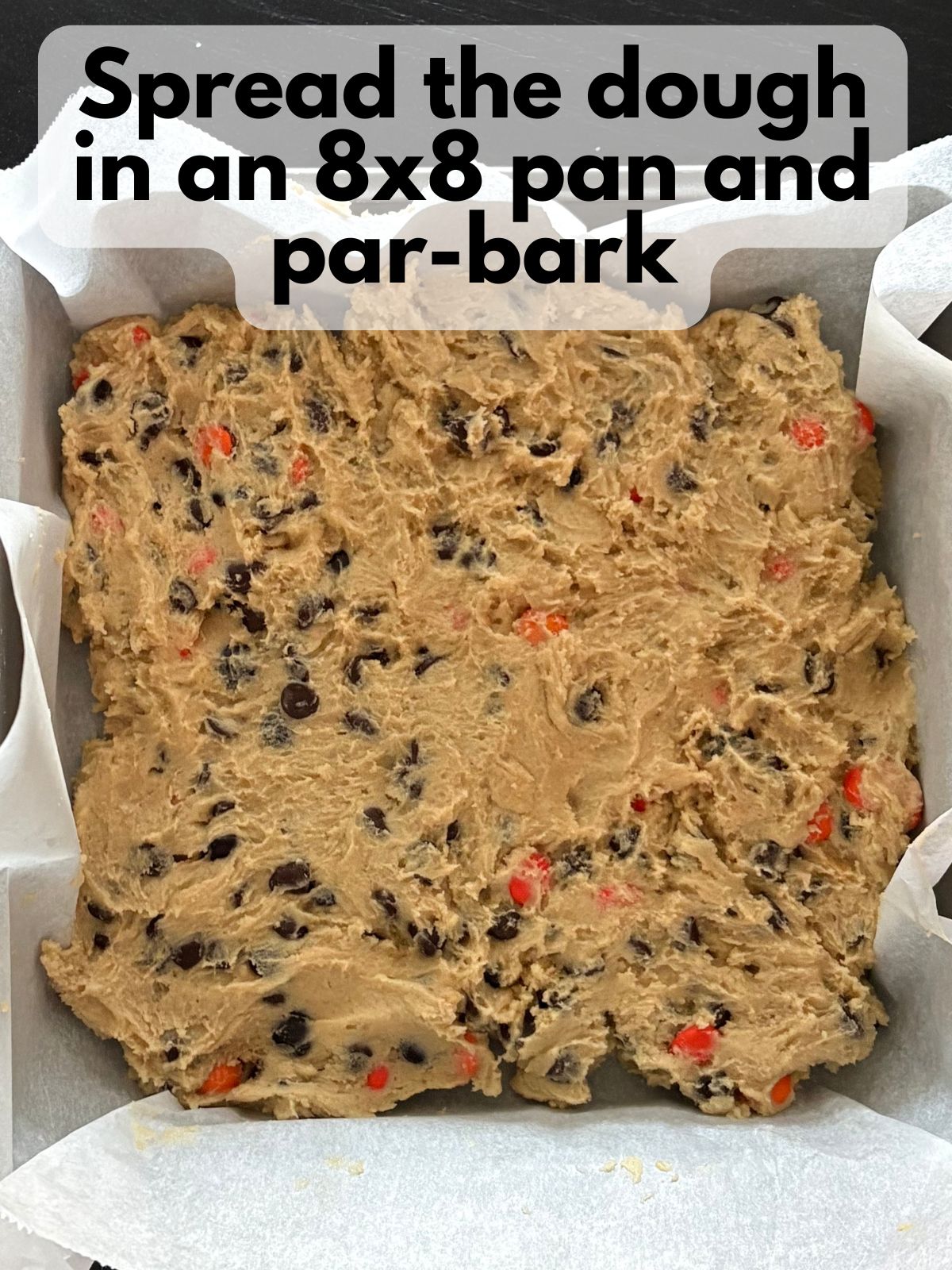 cookie bar dough spread in a square pan lined with parchment paper