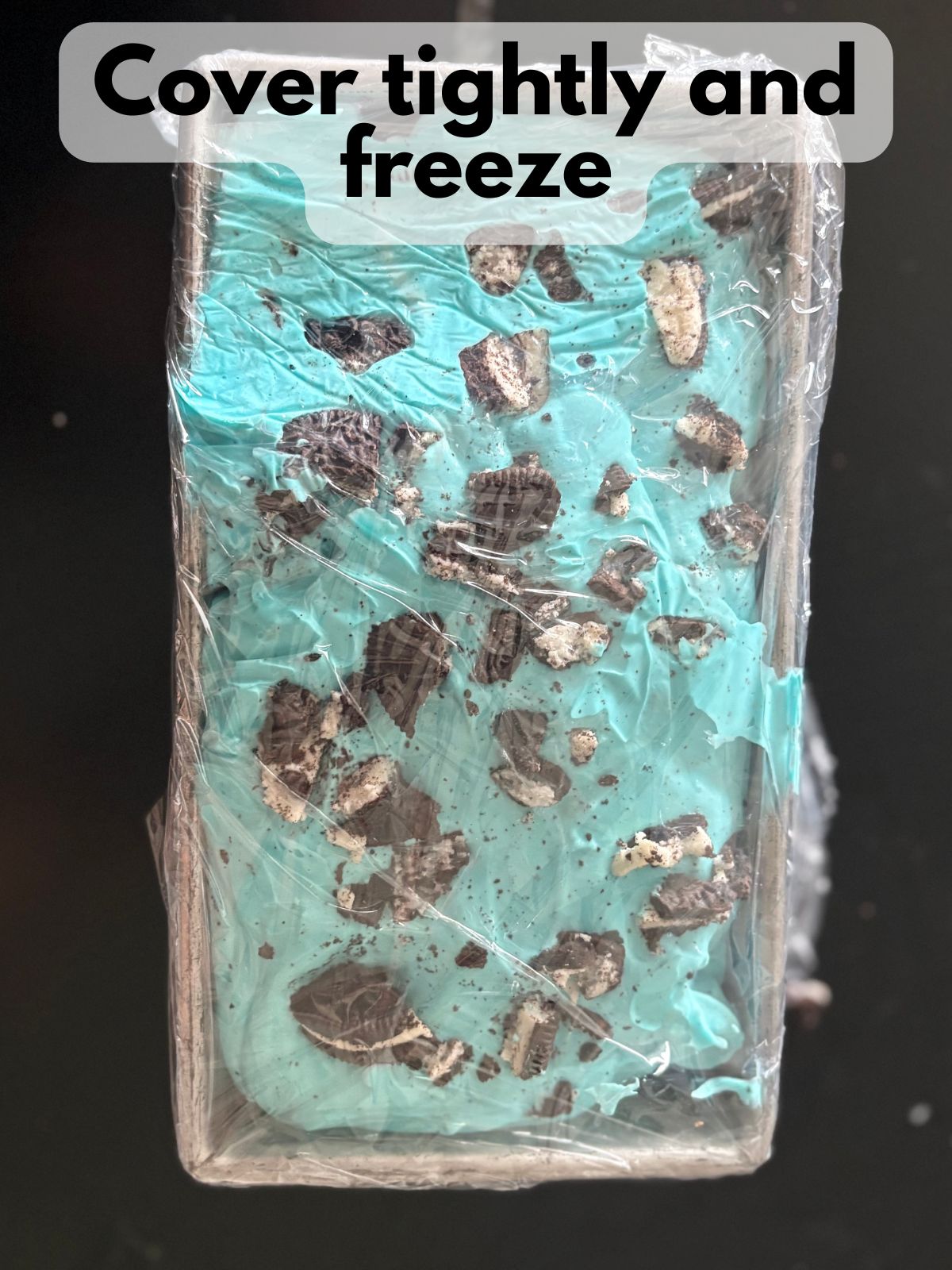 blue oreo ice cream in a loaf pan covered with plastic wrap