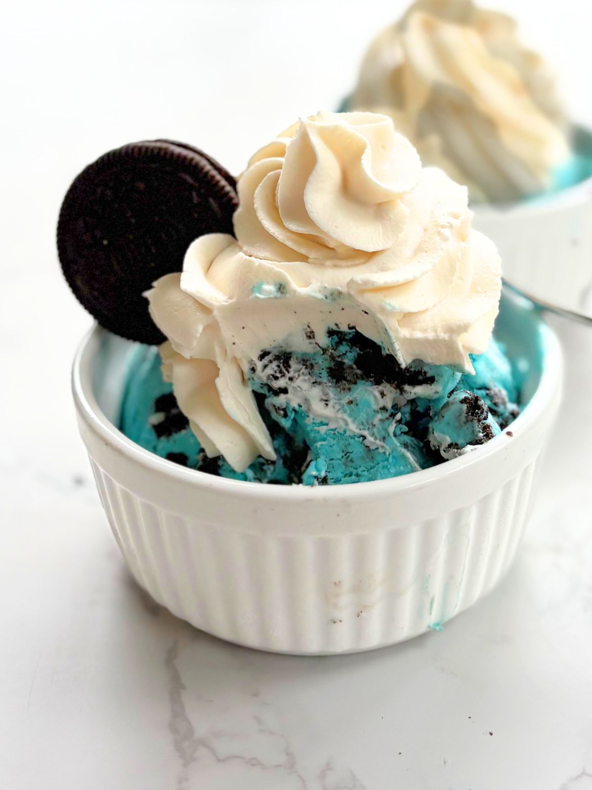 blue oreo ice cream in a bowl with whipped cream and an extra oreo on top
