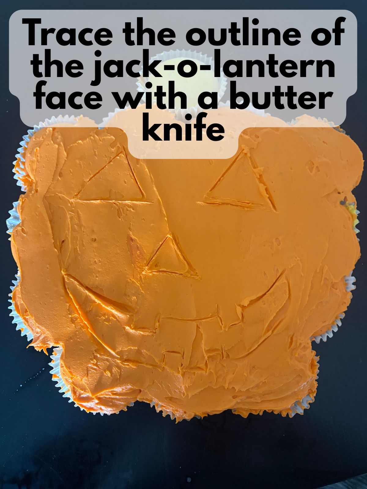 jack-o-lantern face sketched into orange buttercream on a pumpkin-shaped cupcake cake
