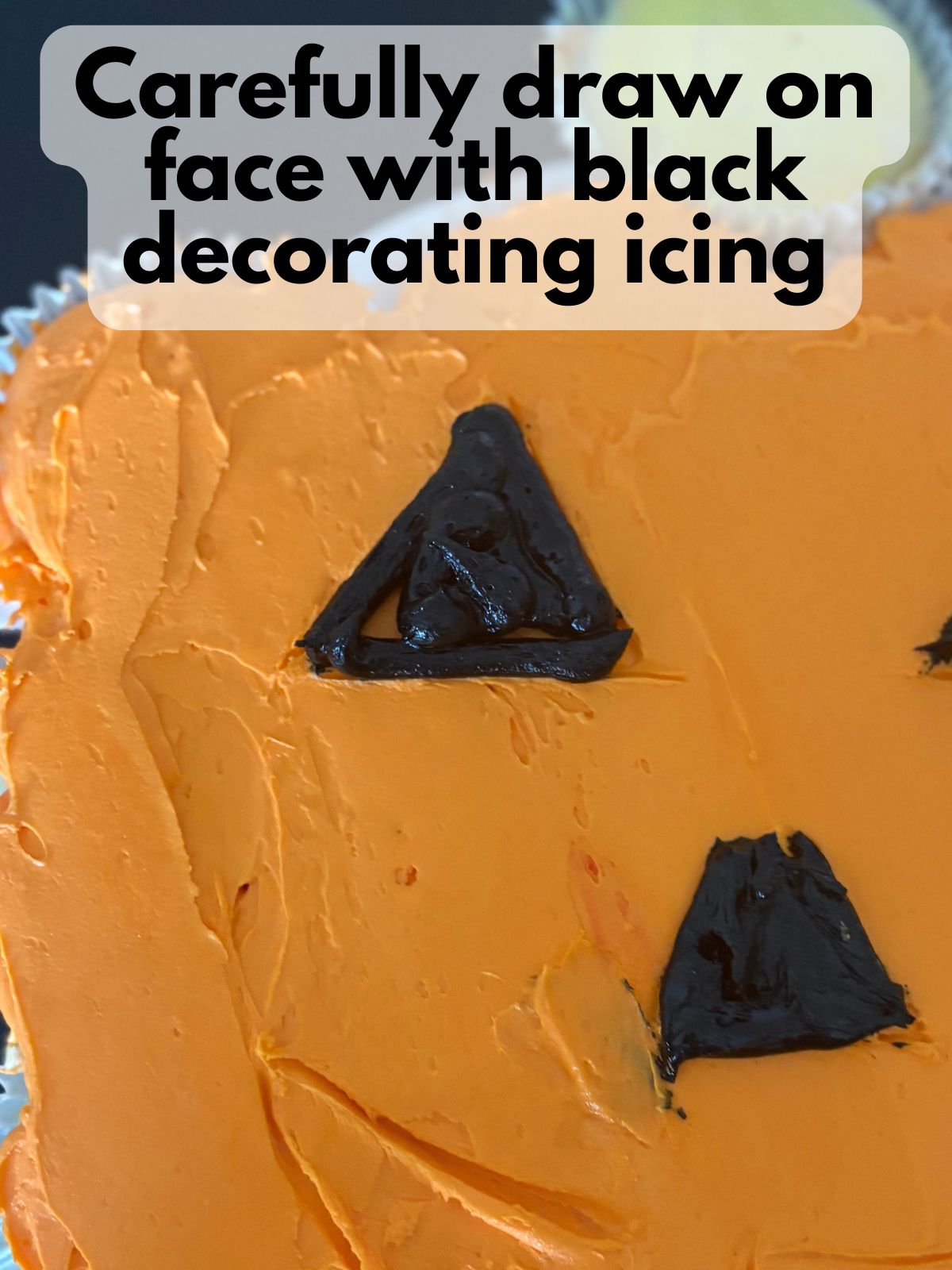 black decorating icing on a pumpkin cupcake cake to form a face