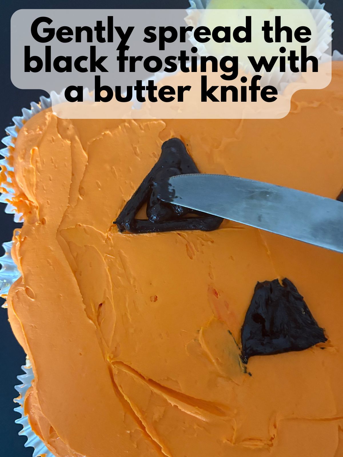 a butter knife smoothing black decorating icing to form the face of a jack-o-lantern