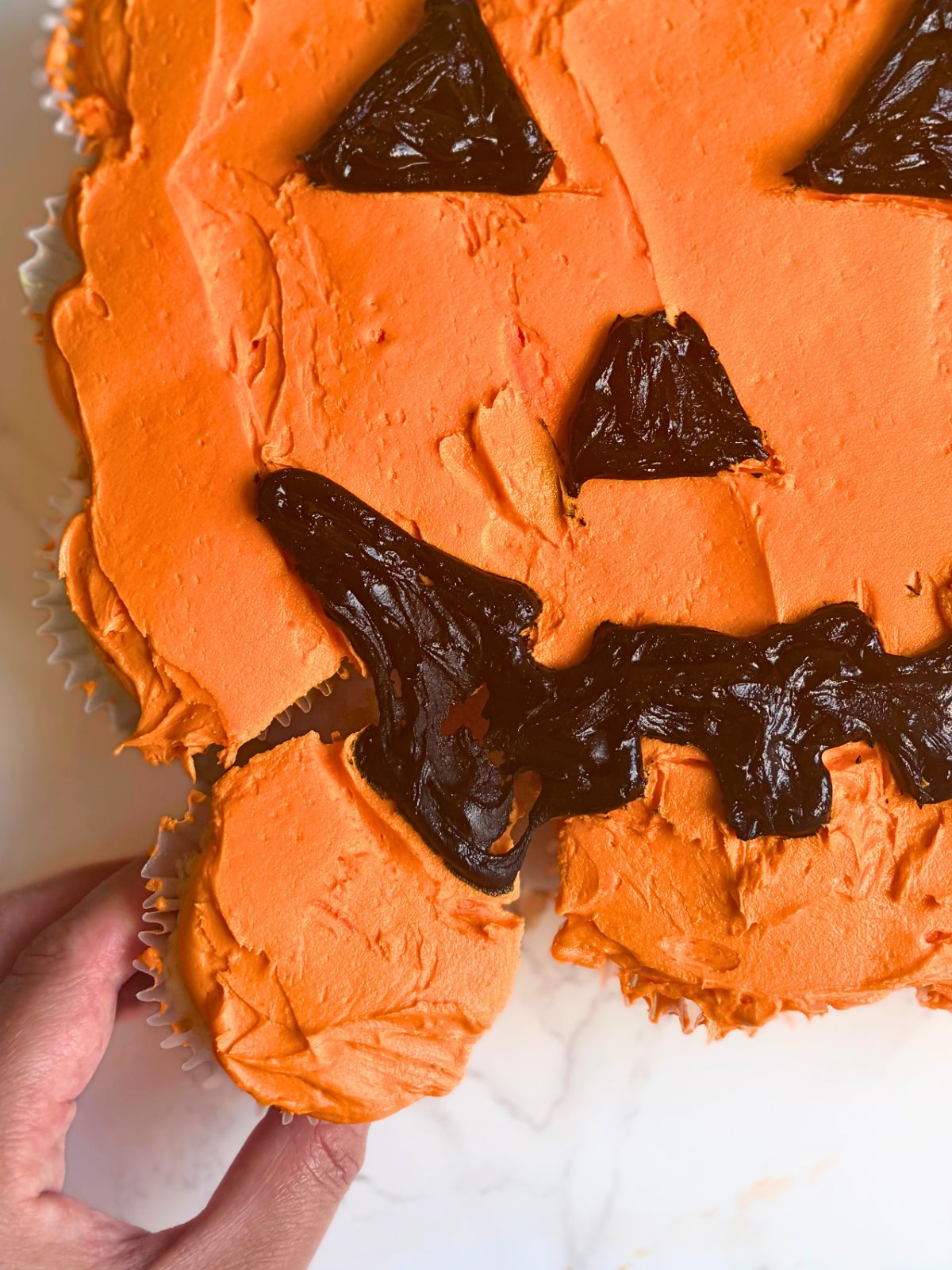 a cupcake being pulled away from a jack-o-lantern cupcake cake