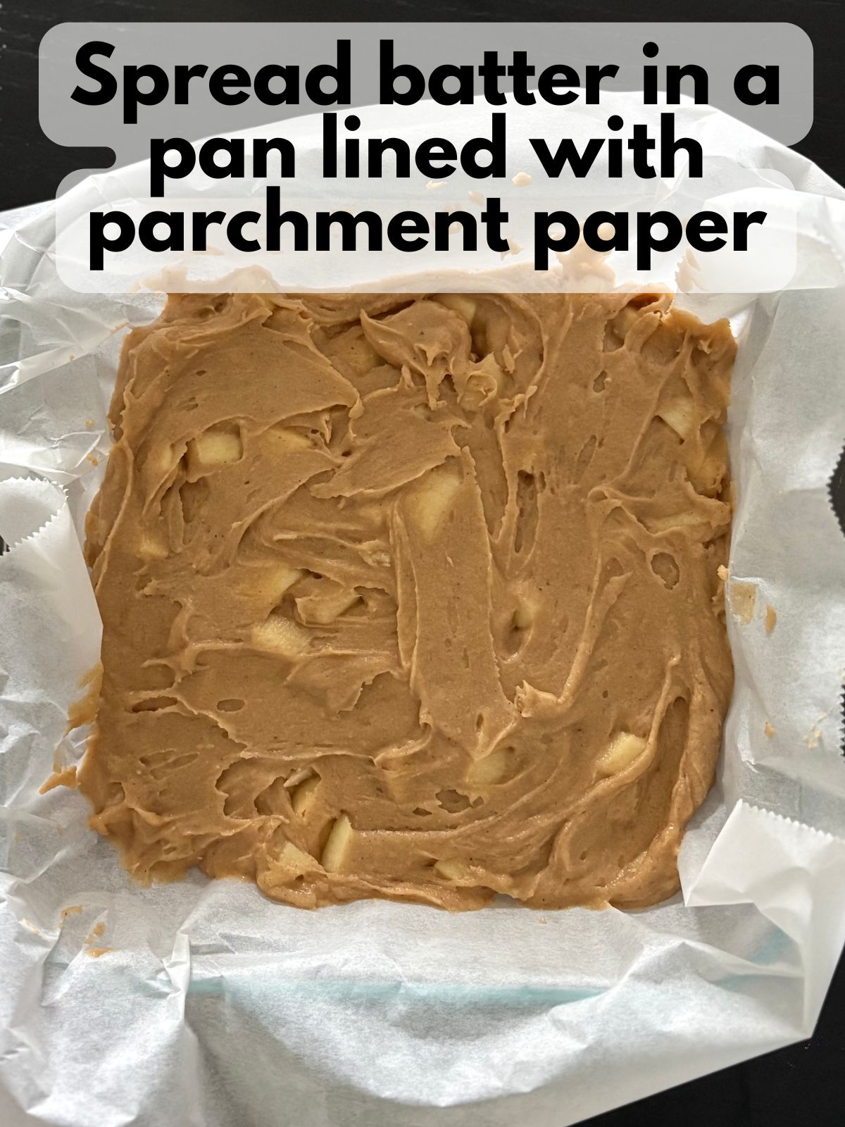 apple blondie batter spread in a pan lined with parchment paper