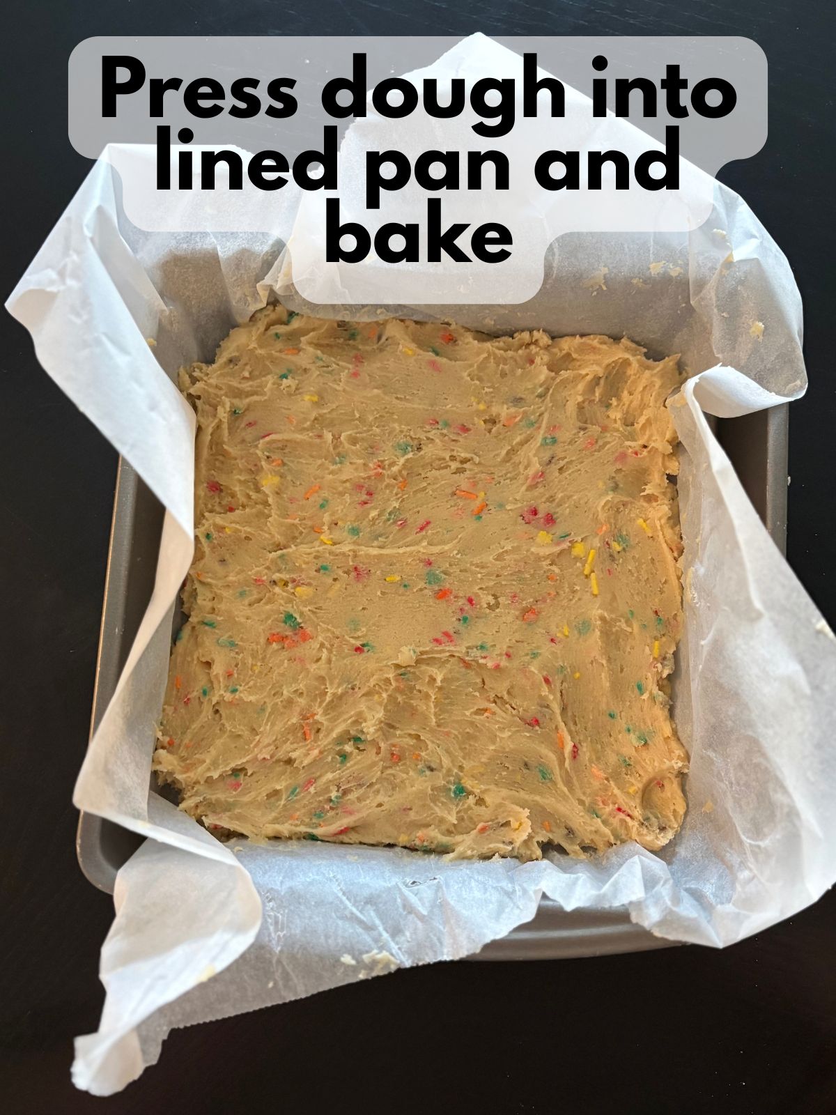 cookie bar dough pressed into a square pan lined with parchment paper