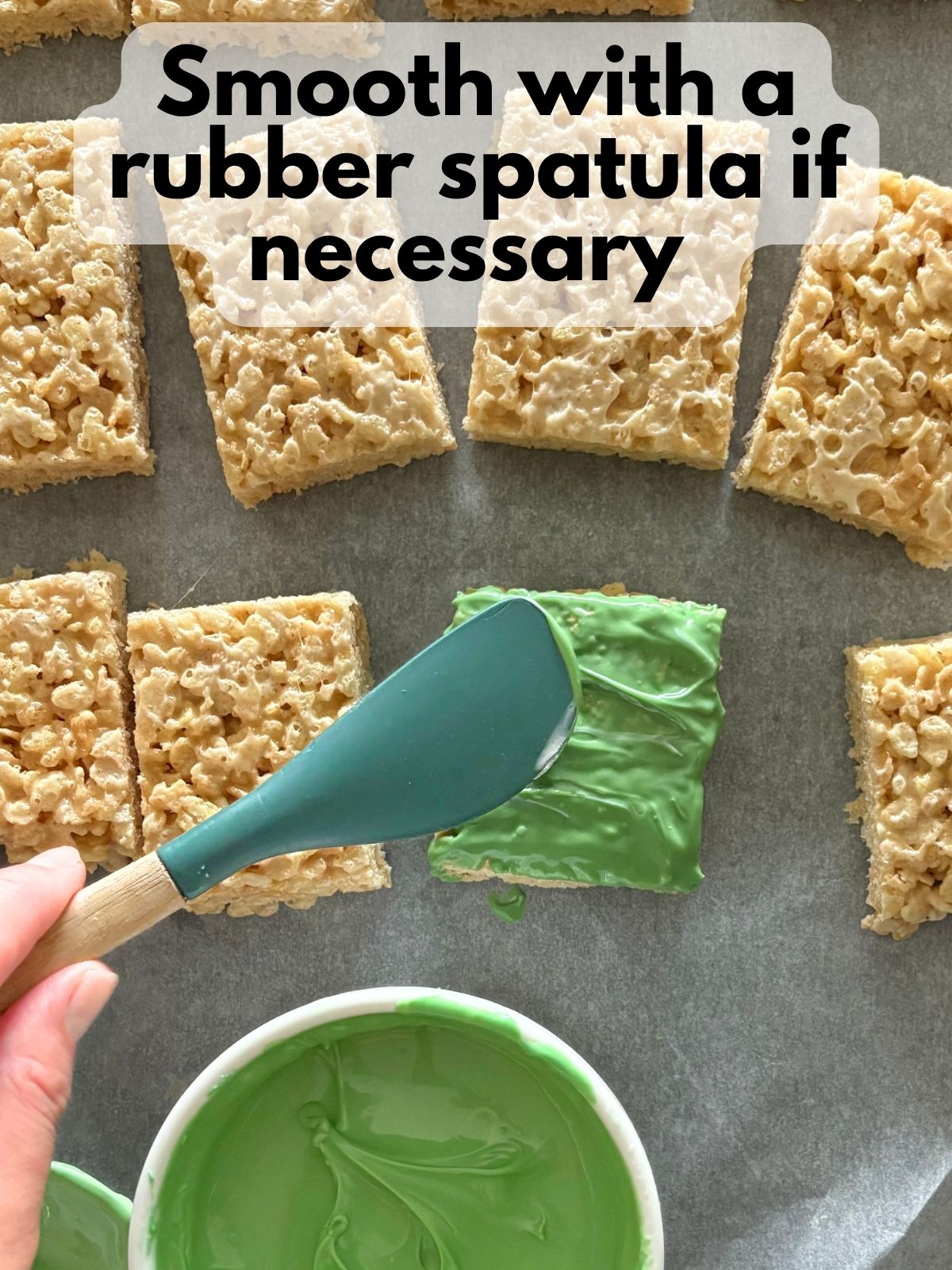 a rubber spatula smoothing melted green candy melt coating a rice krispie treat